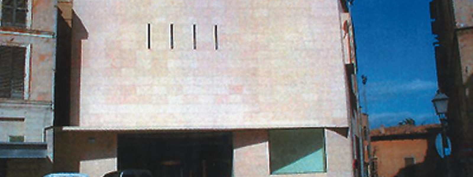 Vista frontal de la Biblioteca Pública del Estado en Palma de Mallorca: bloque cuadrado de fachada ocre junto a la iglesia de Santa Creu.