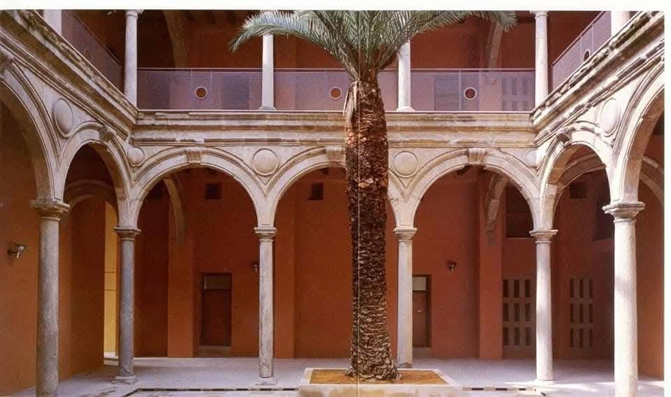 Patio principal del antiguo Convento de Santa Catalina, en Baeza, tras la rehabilitación: arcadas de piedra, columnas dóricas, muros ocres y palmera central.